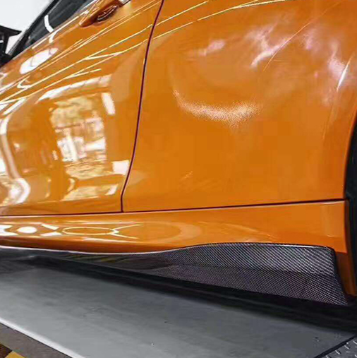 Side sill of an orange BMW M3/M4, close-up, with fitted carbon side skirt (3D Style V2)