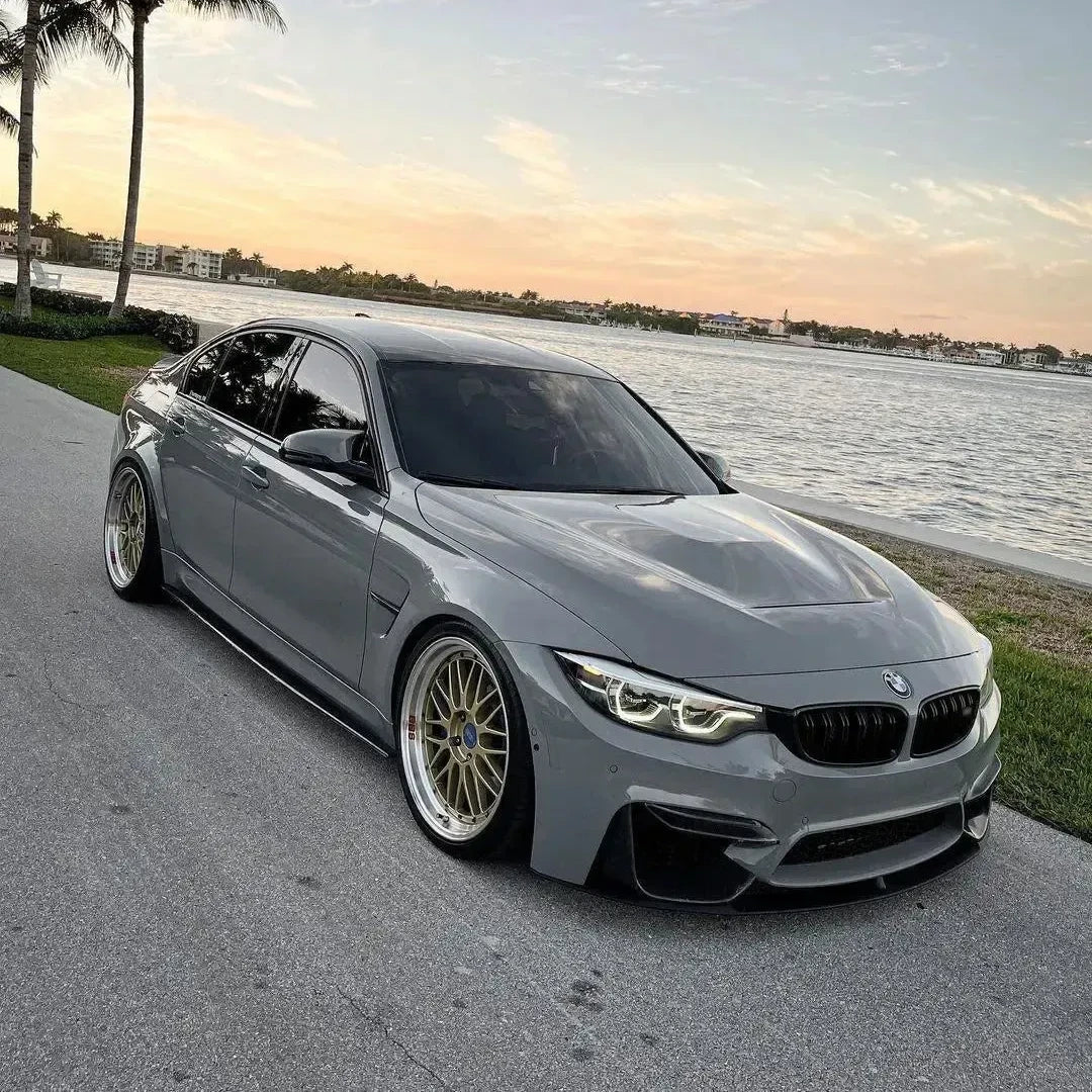 Gray BMW F80 M3 sedan, front angled view by the water, with carbon side skirts (MP Style)