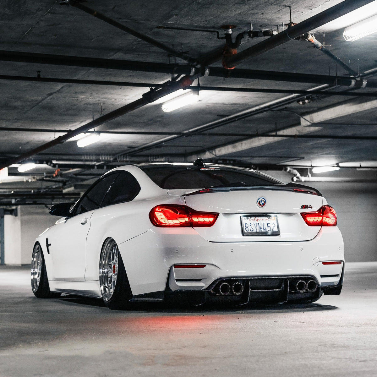 White BMW F82 M4 in a parking garage, angled rear view, with carbon rear diffuser (PSM Style)
