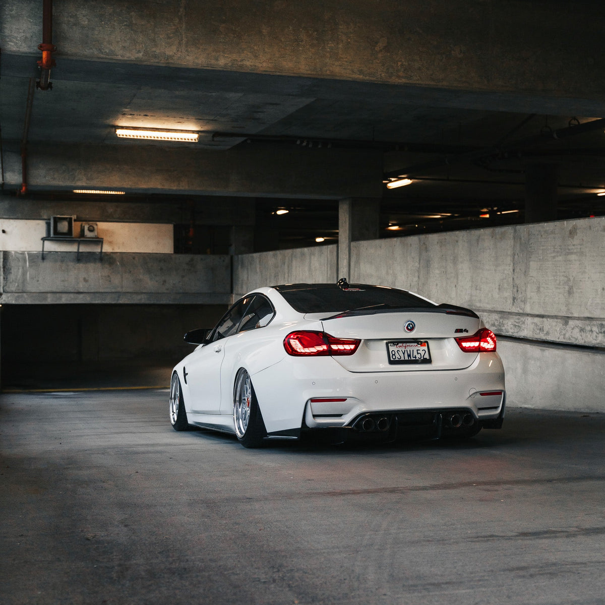 Fehér BMW F82 M4 távolról, parkolóházban, LED féklámpás carbon hátsó diffúzorral (PSM Style)