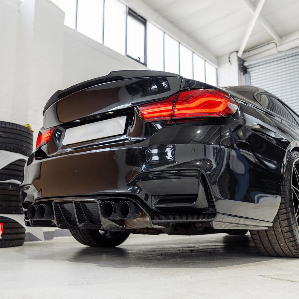 Fekete BMW F82 M4 alacsony, ferde hátulnézetben a műhelyben, carbon diffúzorral (V Style)