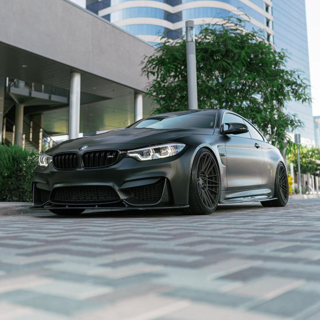 Matte black BMW F82 M4 from a low angle, angled front, with carbon front lip (3D Style)