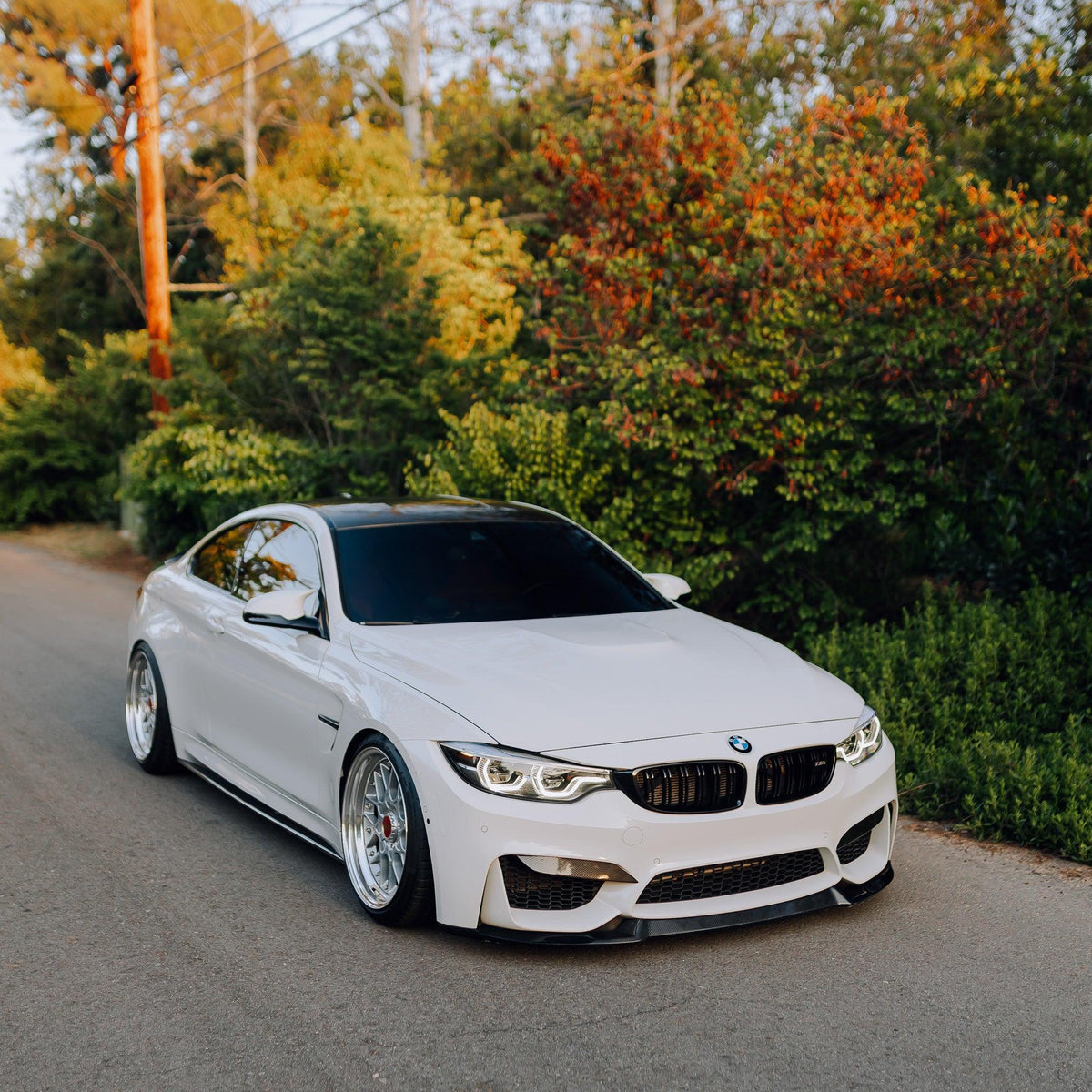 White BMW F82 M4 on the road, angled front view, with carbon fiber front lip (CS Style)