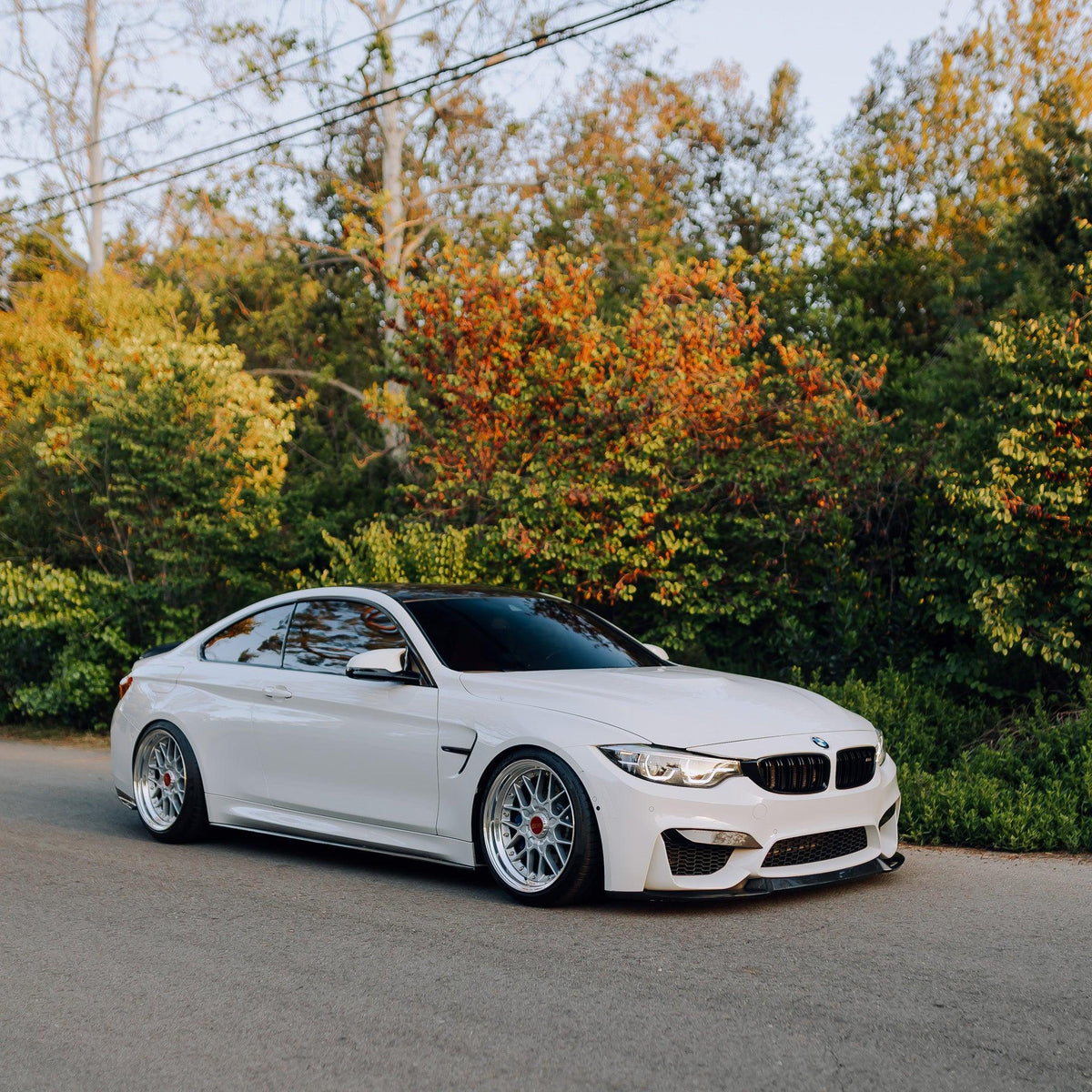 White BMW F82 M4 in half profile on the road, with carbon front lip (CS Style)