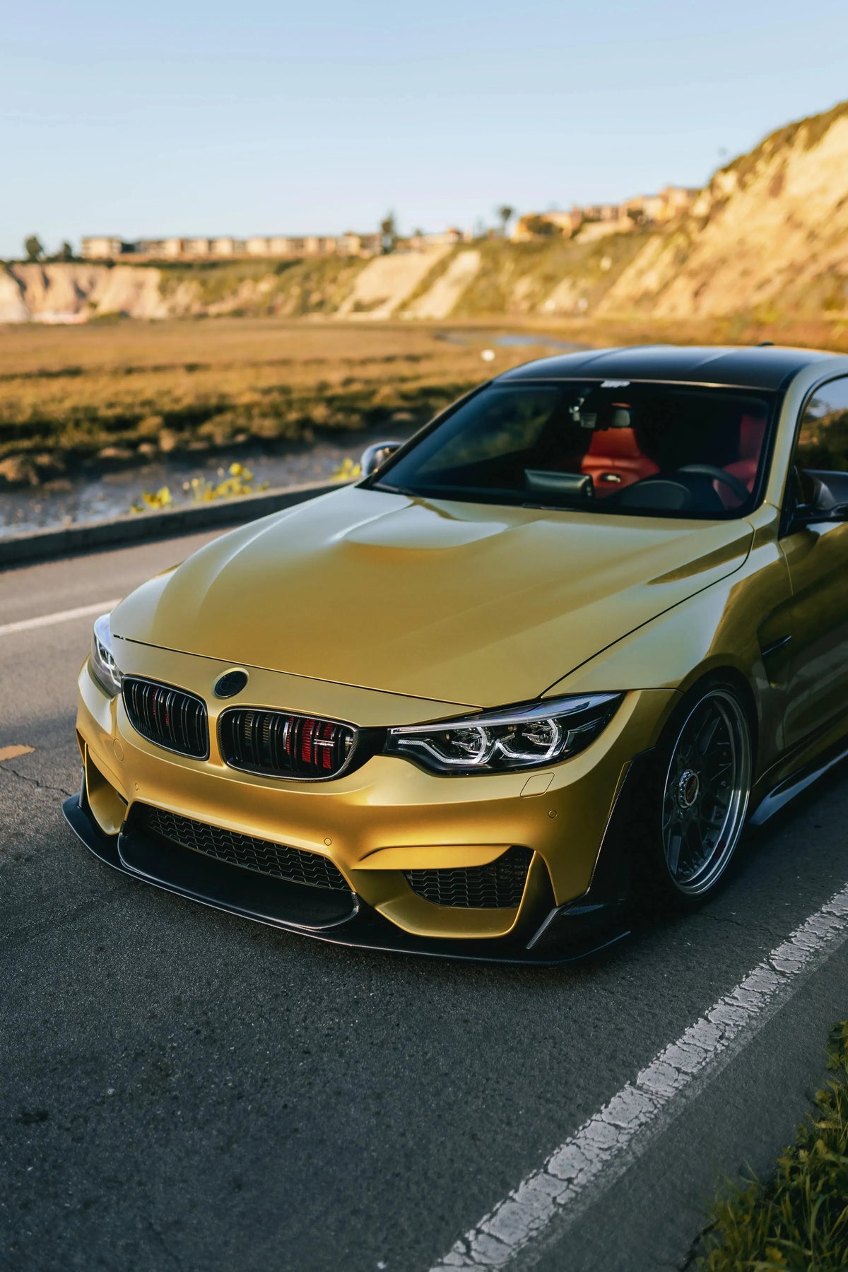 Yellow BMW F82 M4 at the seaside, angled front view, with carbon front lip (Laptor Style)