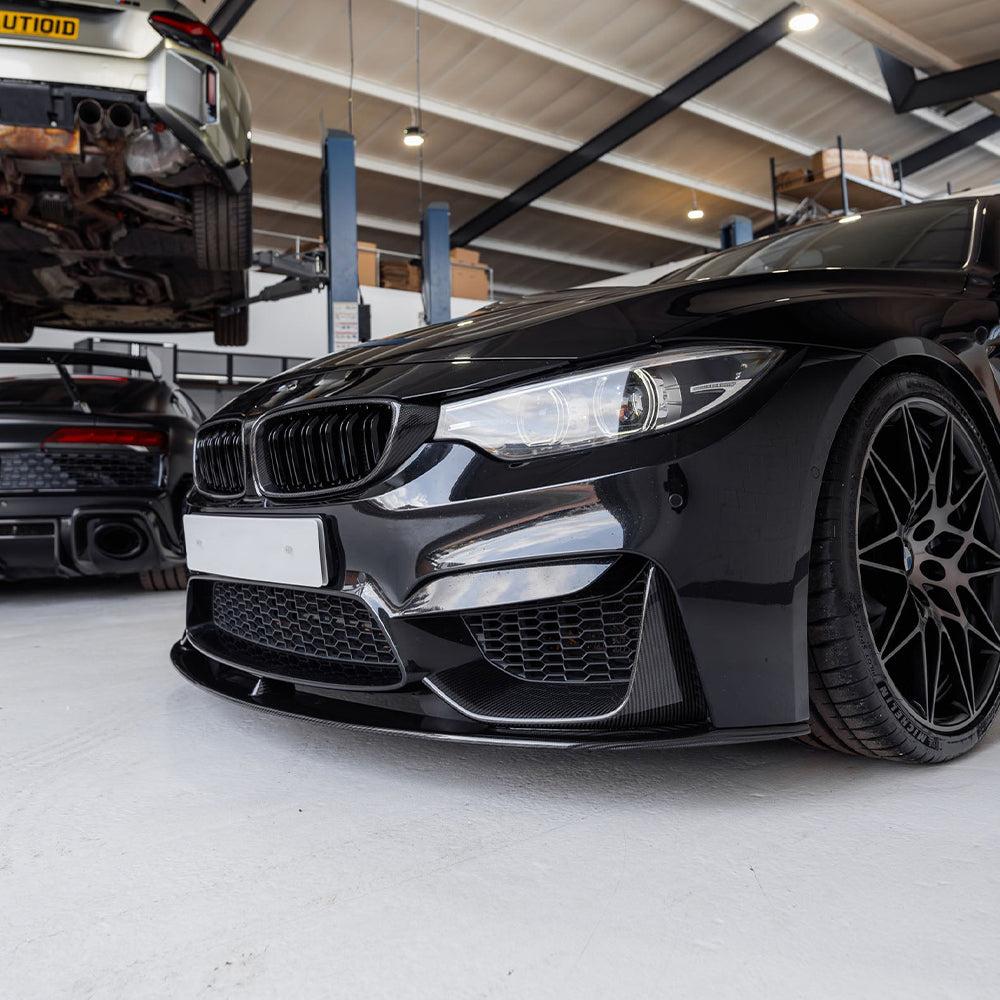 Black BMW F82 M4 front from a low angle in the workshop, with carbon front lip (MP Style)