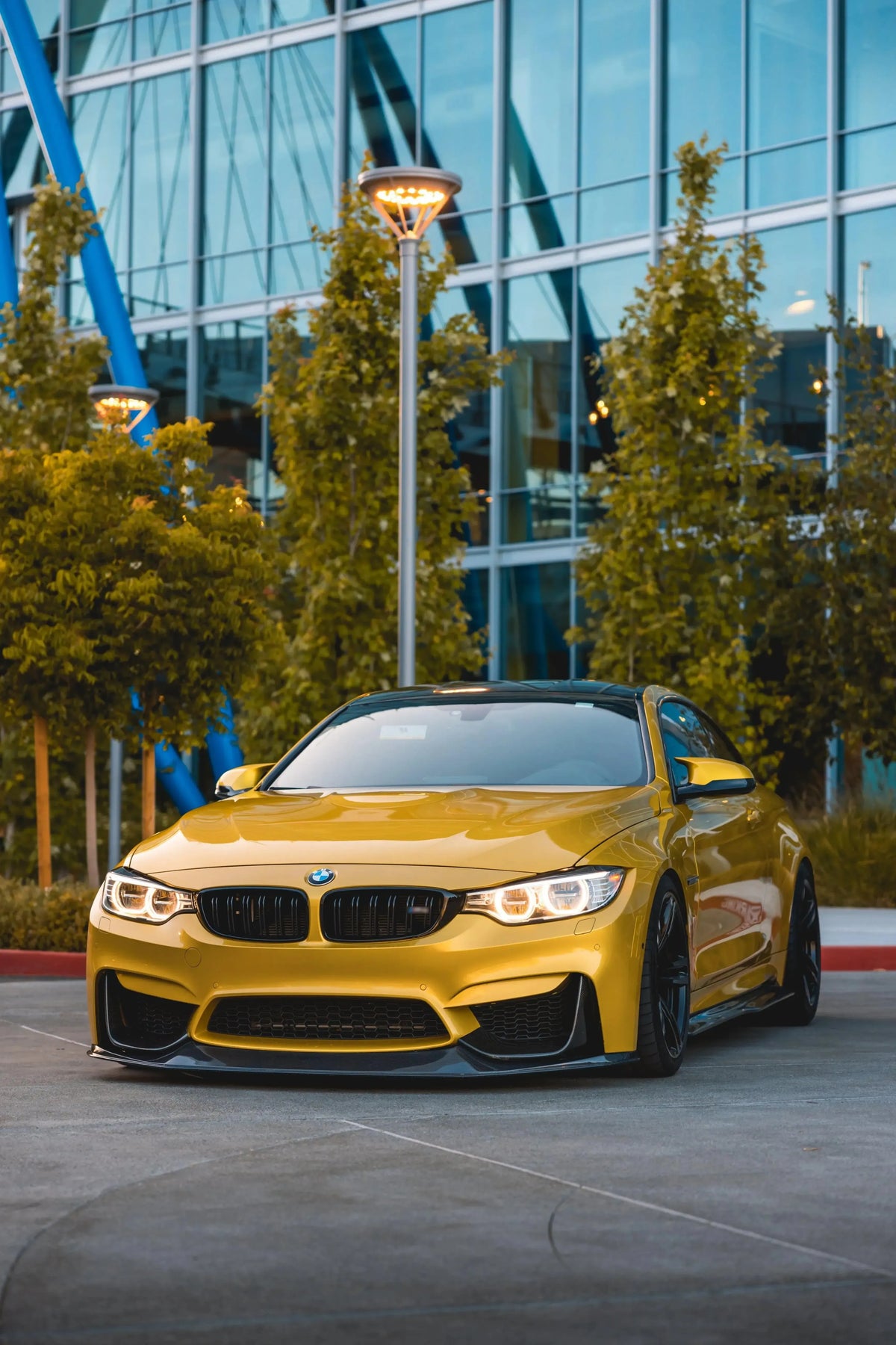 Yellow BMW F82 M4 in front of a glass building, angled front view, with carbon front lip (RSC Style)