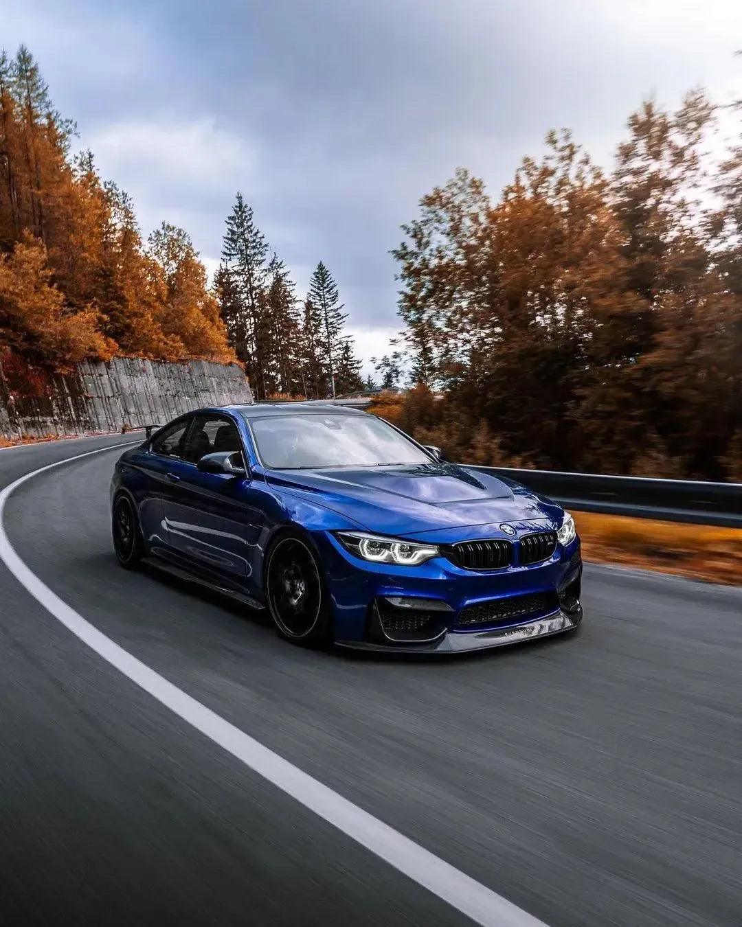 Blue BMW F82 M4 rolling on an autumn road, angled front, with carbon front lip (RSC Style)