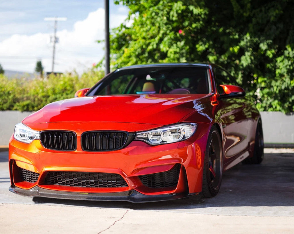 Carbon fiber front lip (V Style) on an orange BMW F82 M4, three-quarter front view
