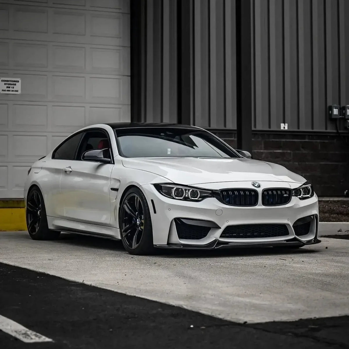 White BMW F82 M4 in front of a garage, angled front view, with carbon front lip (VRS Style)