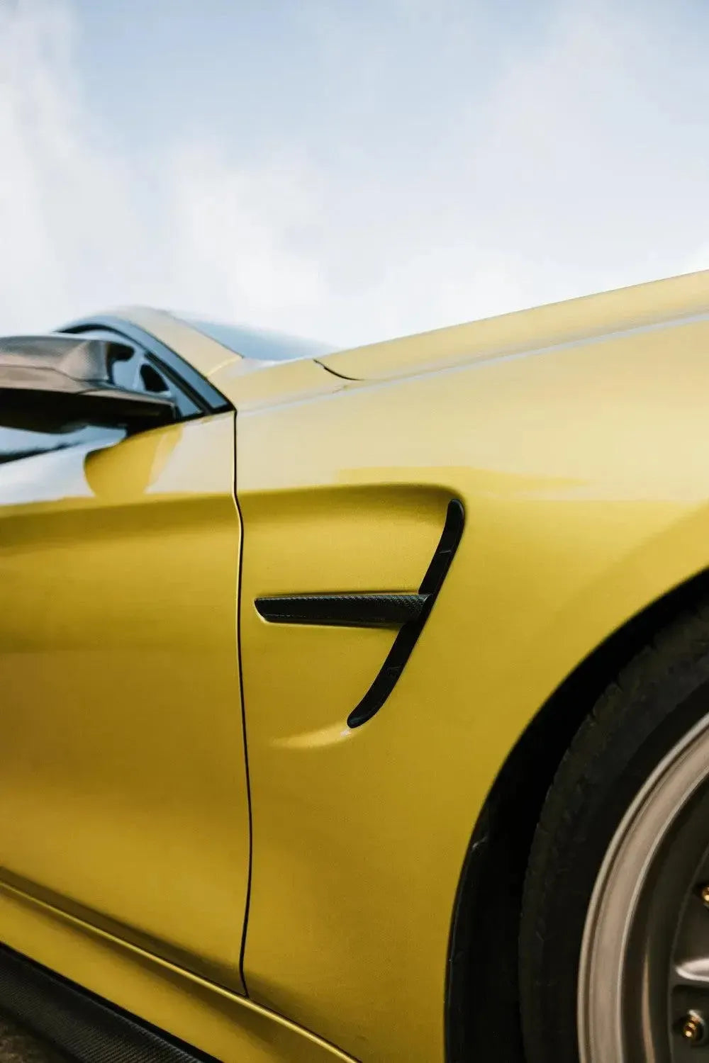 Installed carbon fender vent trim on a yellow BMW F82 M4 fender, low angle