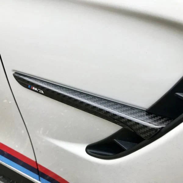 Carbon fender vent trim with M3 badge on the front fender of a white BMW F80 M3