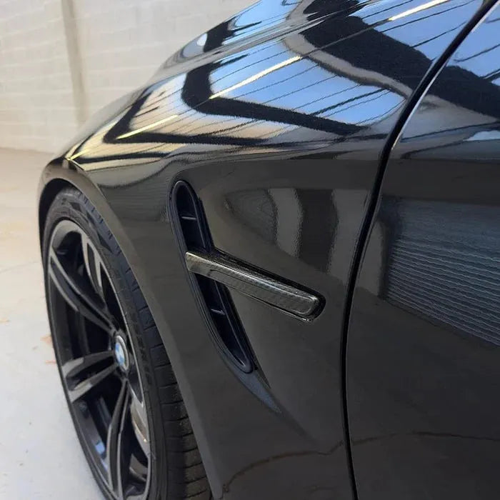 Carbon fender vent trim on the front fender of a black BMW M3/M4, close-up