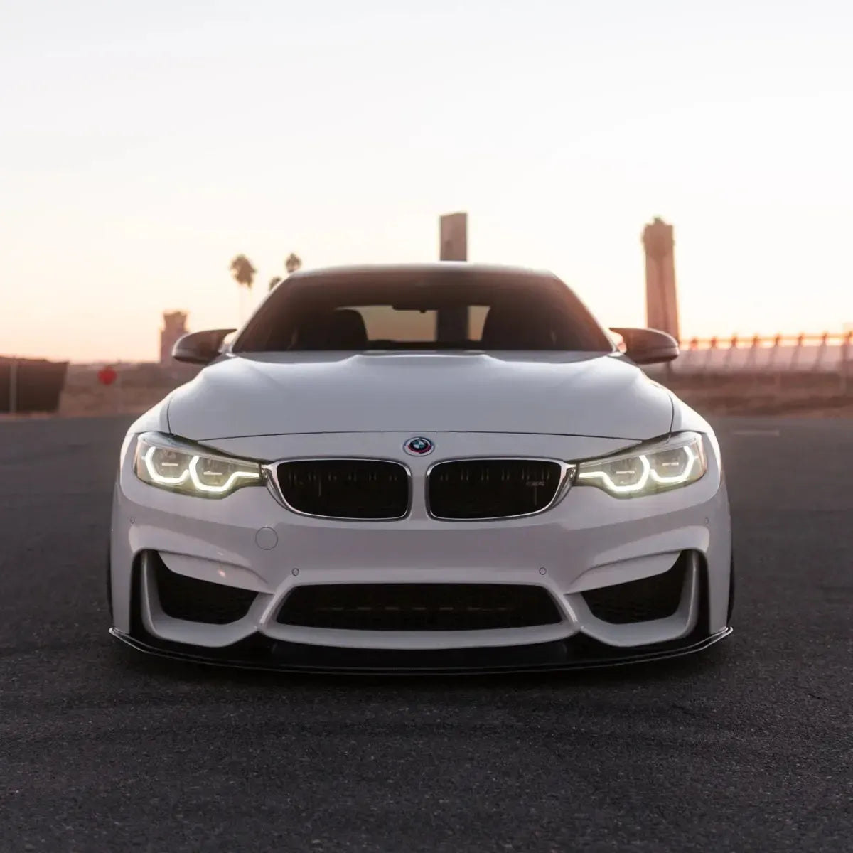 Headlights with warm white DRL on a white BMW F82 M4 at dusk, front view (LCI Ikon Style)