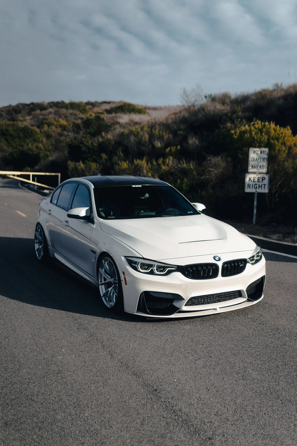 Fehér BMW F80 M3 elölről ferdén az úton, szellőzős alumínium motorháztetővel (GTS Style)