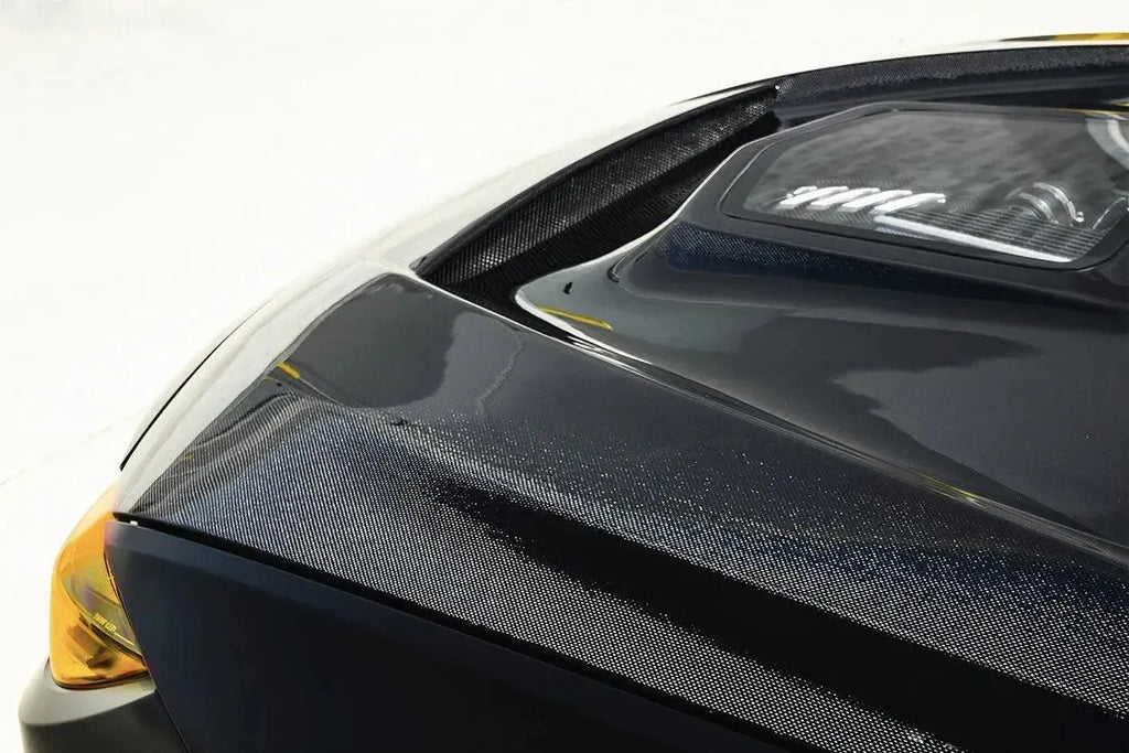 Sárga BMW M3/M4 carbon motorháztetőjének első éle közelről, átlátszó ablakkal (IMP Style)
