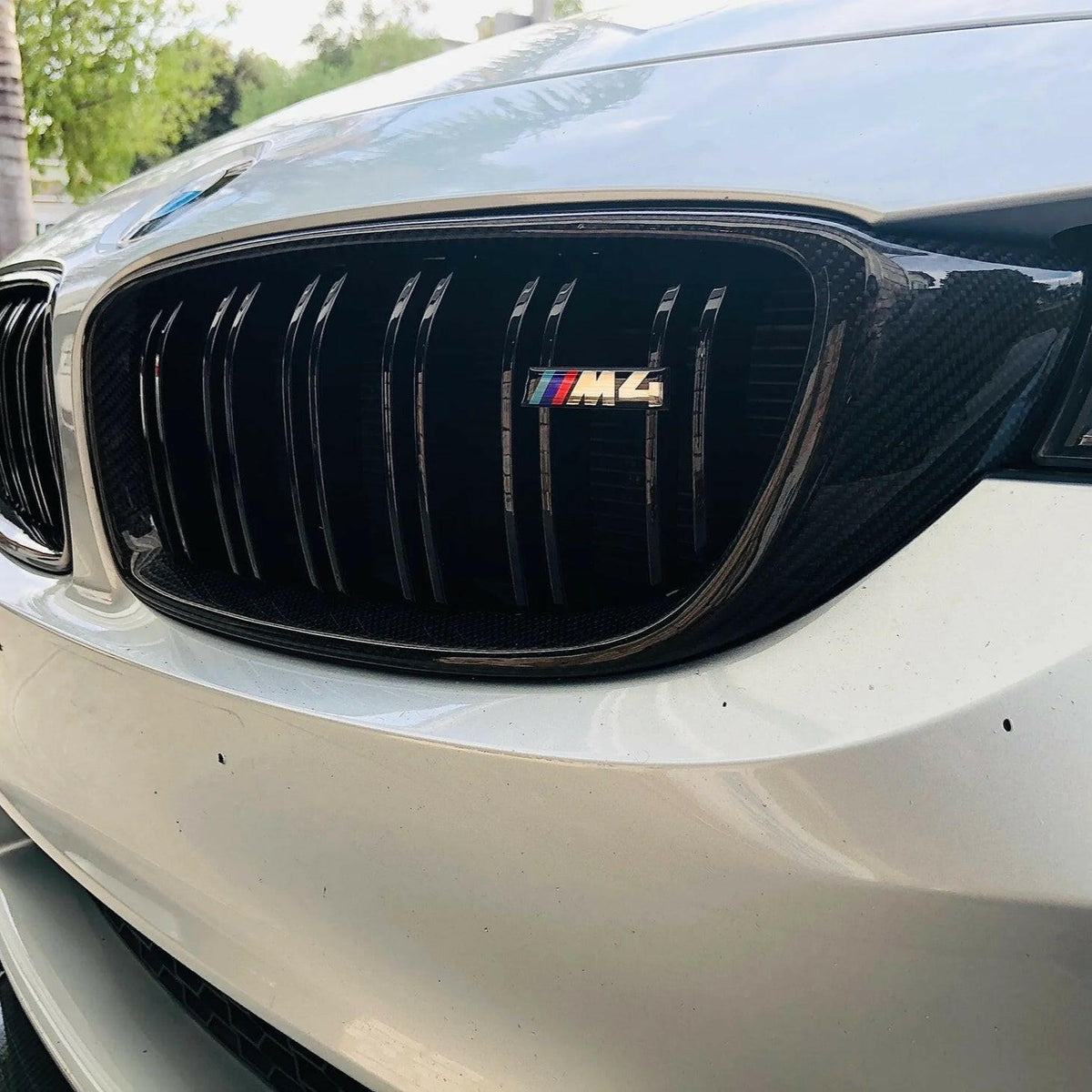 Fehér BMW F82 M4 veséje közelről M4 emblémával: dupla rácsos vese carbon kerettel, fekete rácsokkal