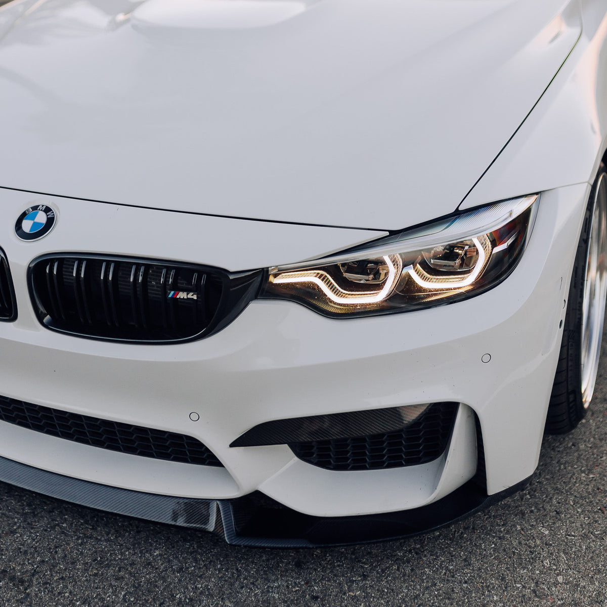 Fehér BMW F82 M4 első sarka közelről, fényes fekete dupla rácsos vesével