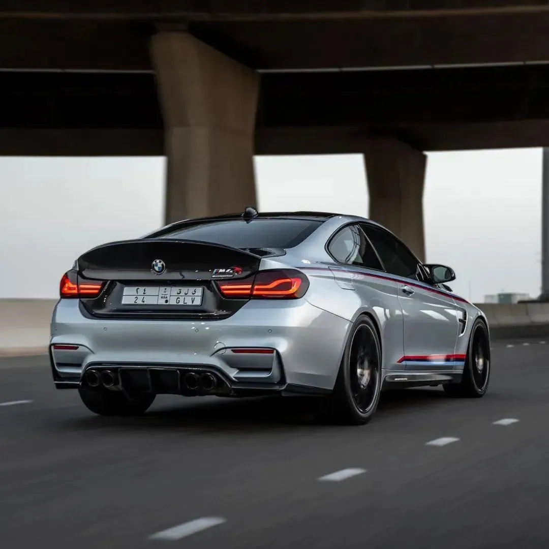 Silver BMW F82 M4 under a bridge, rear three-quarter view with carbon trunk lid (CSL Style)