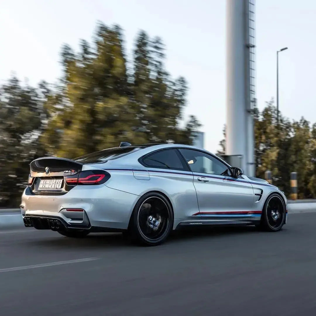 Silver BMW F82 M4 driving on the road, from the side-rear, with fitted carbon trunk lid (CSL Style)