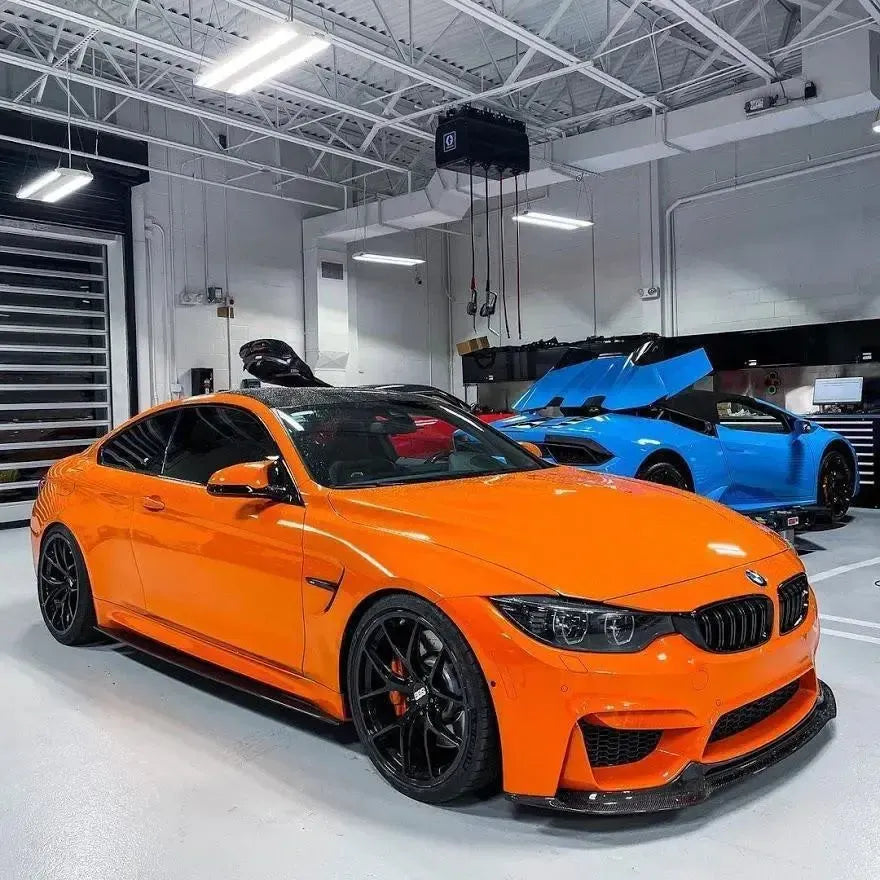 Orange BMW F82 M4 in the workshop, with carbon side skirts, front three-quarter view (MP Style)