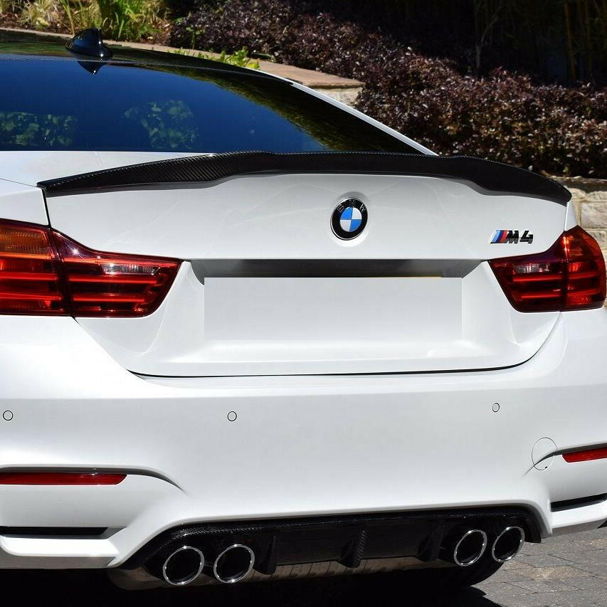 Carbon spoiler fitted on the trunk of a white BMW M4, rear view (M4 Style)