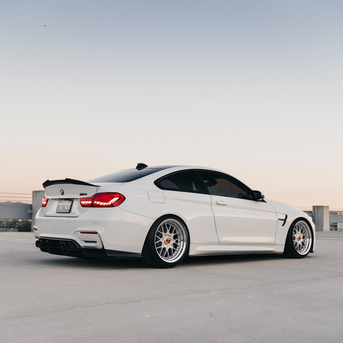 White BMW M4 on a rooftop, rear three-quarter side view with carbon spoiler (PSM Style High Kick)
