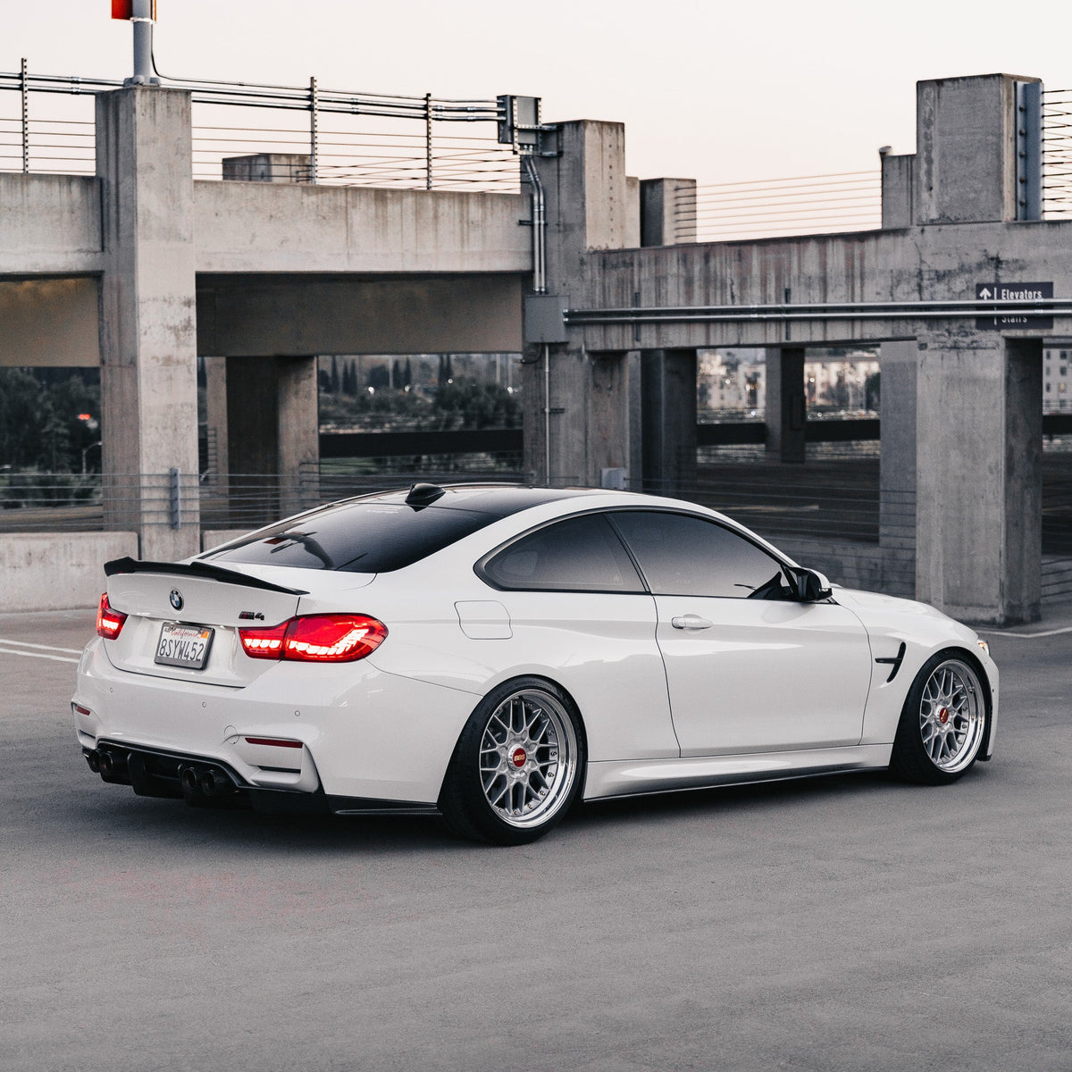 White BMW M4 parked in a parking garage, from the rear, with carbon high kick spoiler (PSM Style High Kick)