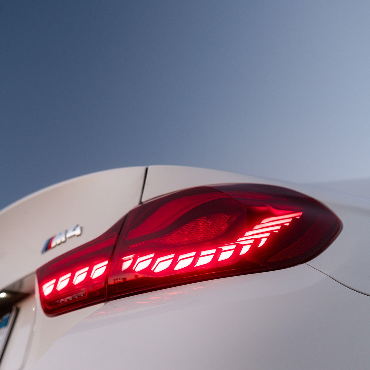 Illuminated red OLED tail light of a white BMW M4, close-up at dusk (GTS Style)