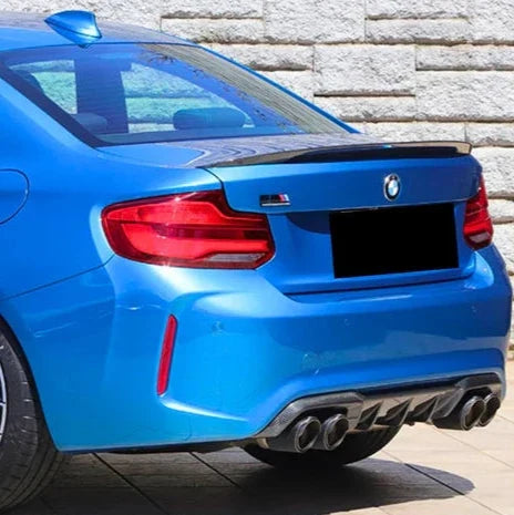 Kék BMW F87 M2 hátulról ferdén kőfal előtt, felszerelt Performance Style carbon diffúzorral