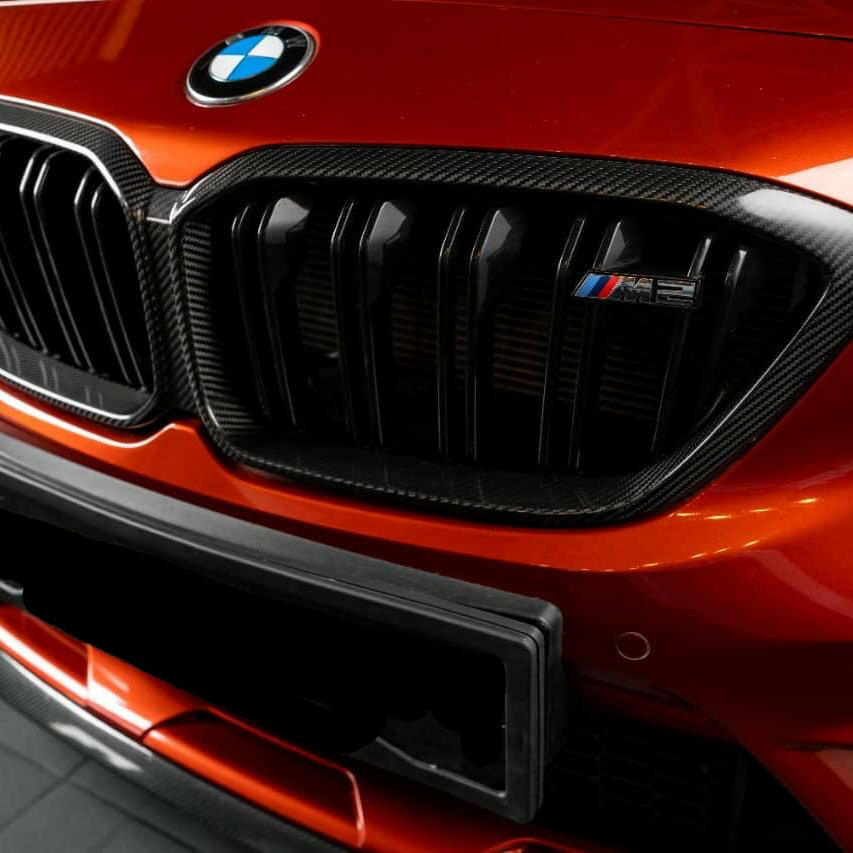 Narancssárga BMW F87 M2 Competition eleje közelről, felszerelt carbon vesekeret-borítással