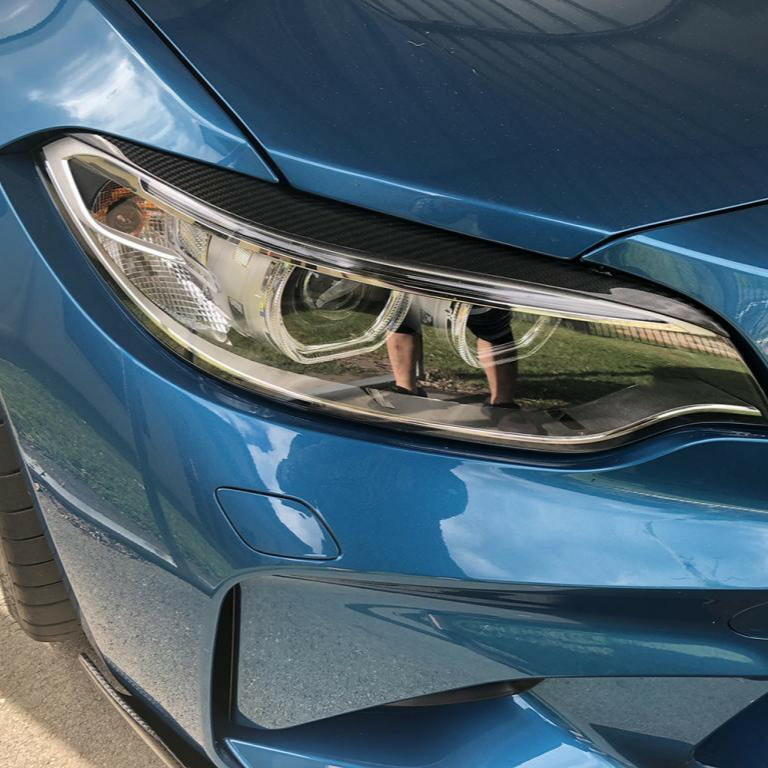 Kék BMW F87 M2 fényszórója közelről, felszerelt carbon szemöldökkel