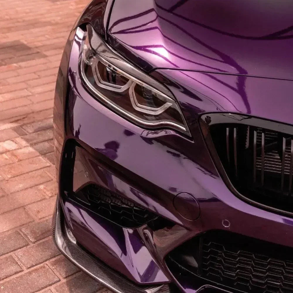 Front corner of a purple BMW F87 M2, close-up, with carbon headlight eyelid