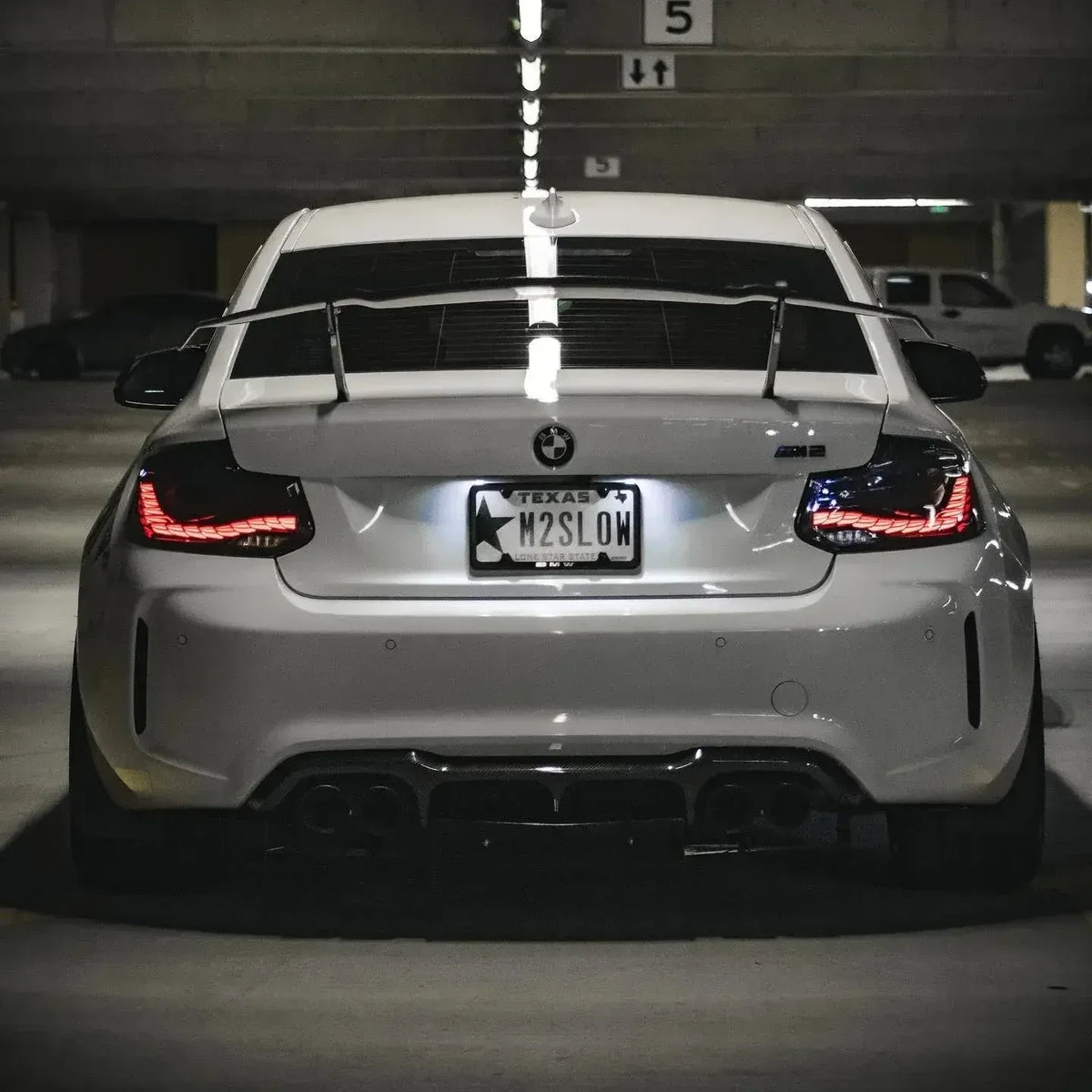 Fehér BMW F87 M2 hátulról parkolóban, világító GTS Style OLED hátsó lámpákkal