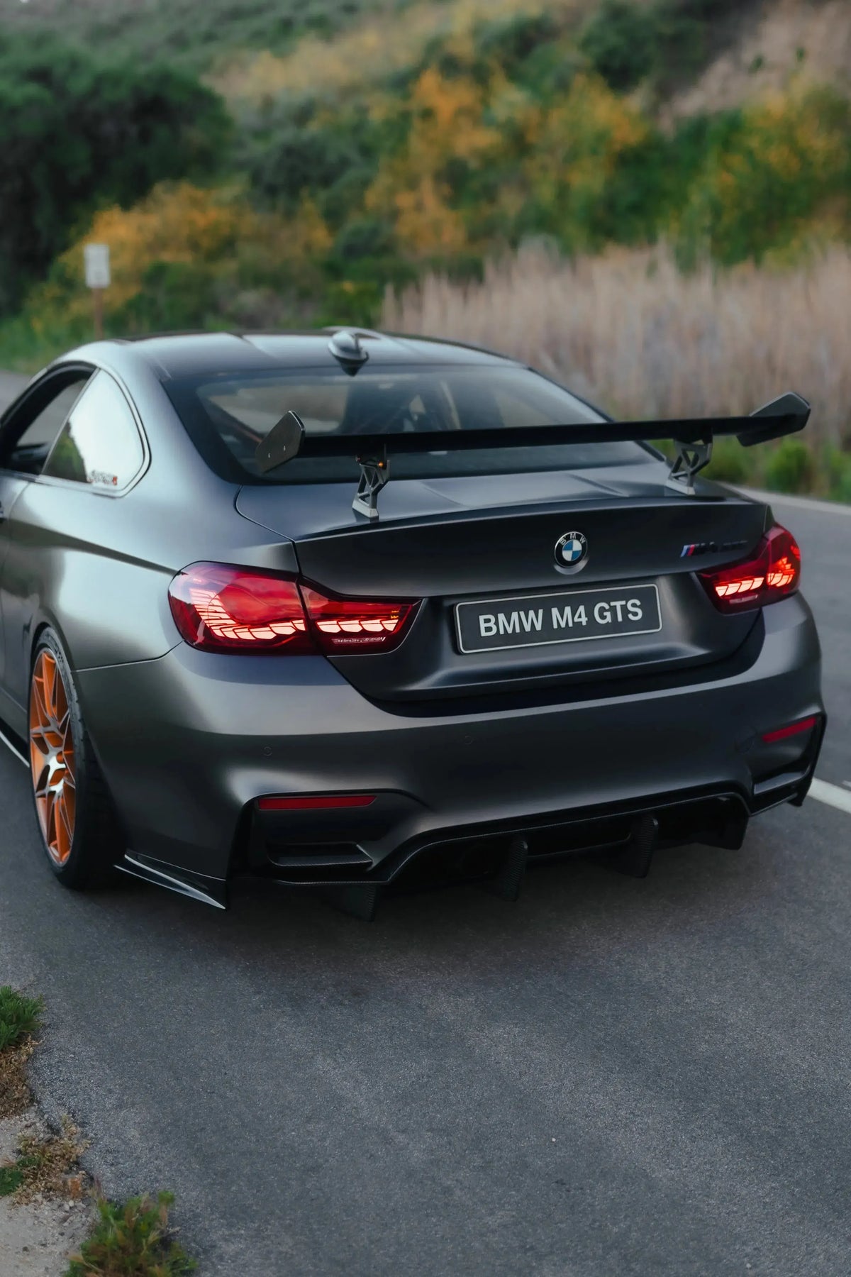 Szürke BMW F82 M4 GTS hátulról ferdén az úton, felszerelt GTS Style carbon hátsó szárnnyal