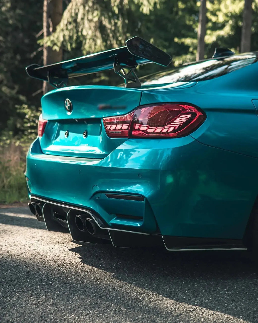 Kék BMW F82 M4 hátulja ferdén, közelről erdőben, GTS Style carbon hátsó szárnnyal