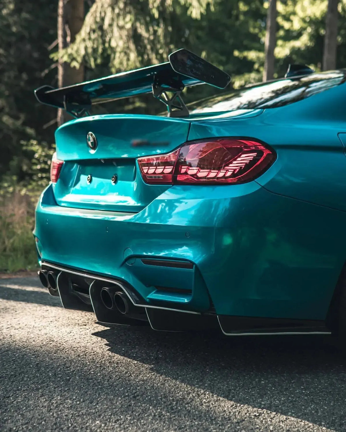 Kék BMW F82 M4 hátulja ferdén, közelről erdőben, GTS Style carbon hátsó szárnnyal