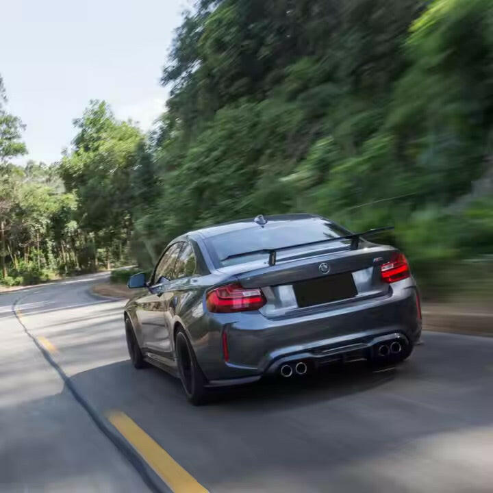 Szürke BMW F87 M2 hátulról ferdén menet közben, felszerelt Low Pedestal Style carbon hátsó szárnnyal