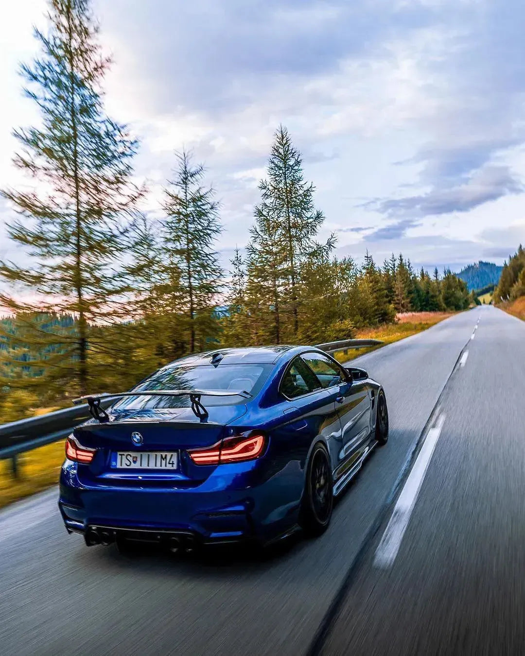 Kék BMW F82 M4 hátulról hegyi úton, felszerelt V Style forged carbon hátsó szárnnyal