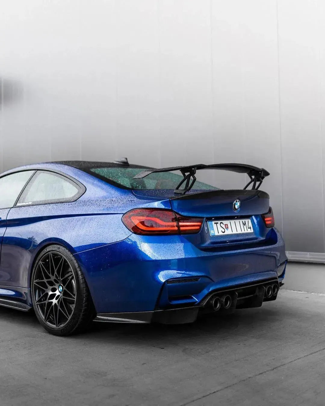Kék BMW F82 M4 hátulról ferdén stúdióban, felszerelt V Style forged carbon hátsó szárnnyal