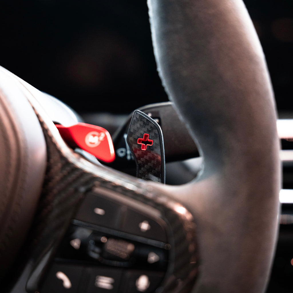 Carbon “+” paddle shifter with red marking fitted on a BMW G Series M steering wheel, close-up