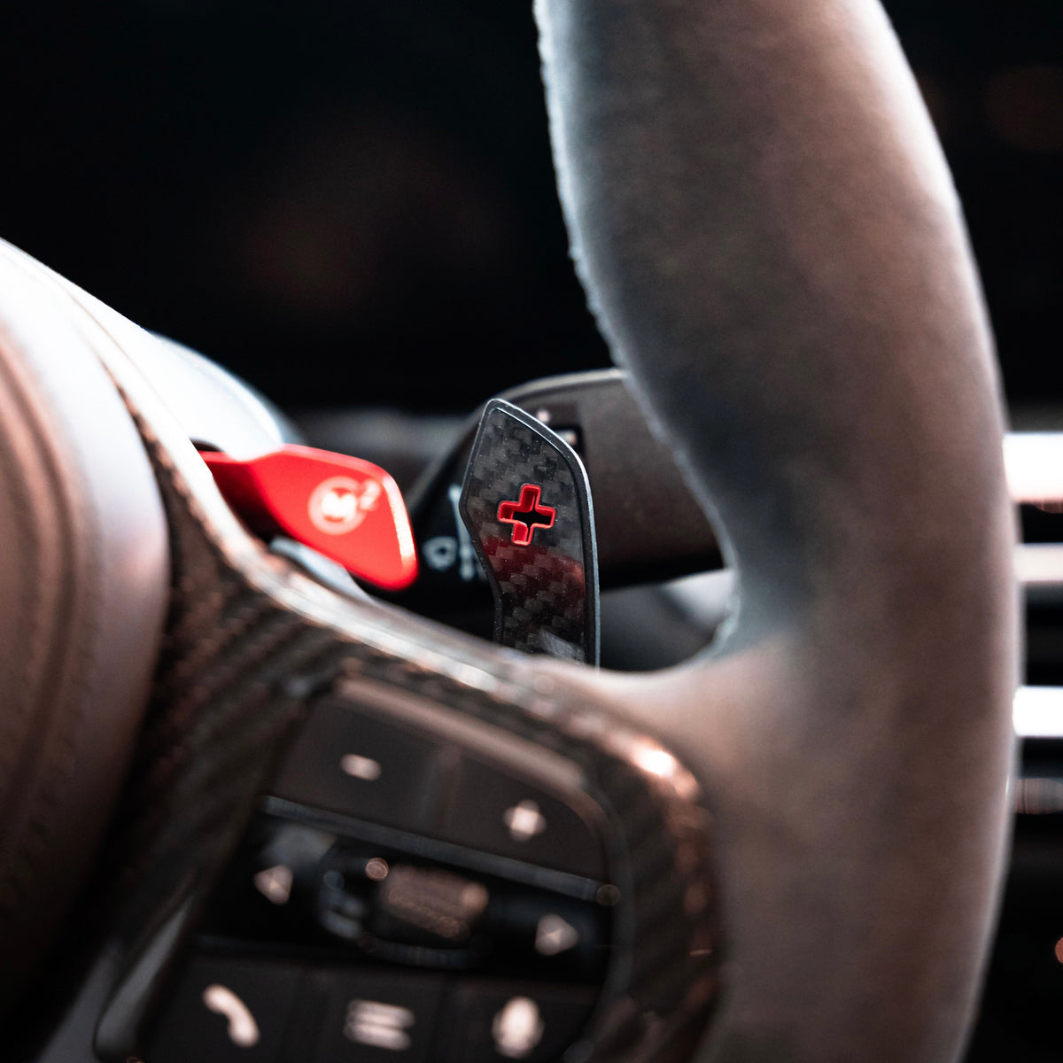 Carbon “+” paddle shifter with red marking fitted on a BMW G Series M steering wheel, close-up