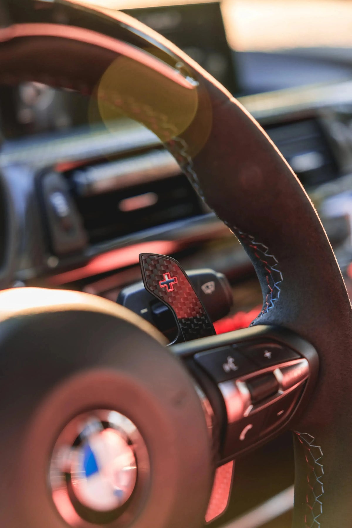 Carbon paddle shifter with red + marking, fitted behind an Alcantara steering wheel (MP Style) – BMW G87 M2 / G80 M3 / G82 M4