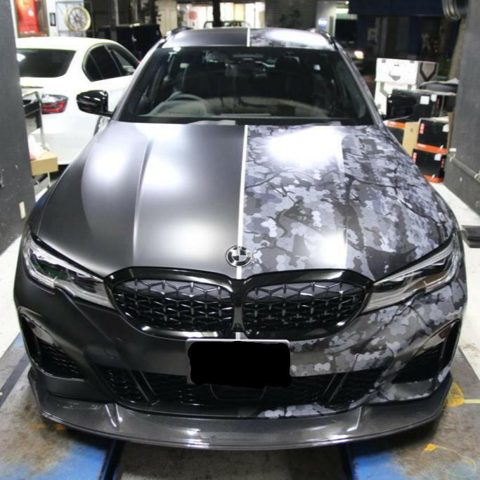 Gray camouflage-wrapped BMW G21 Touring head-on, with fitted carbon front lip (Euro Style V4)