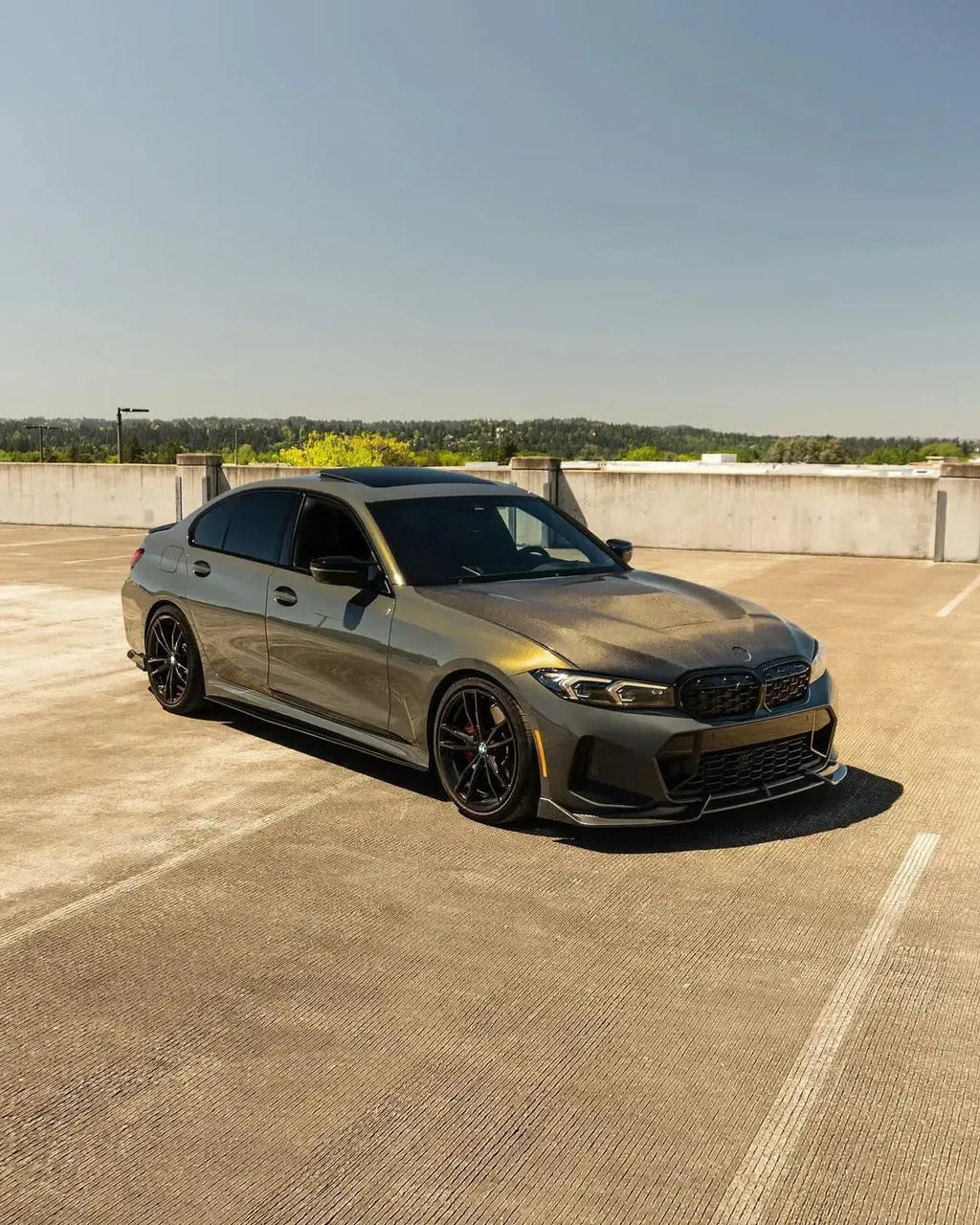Matte olive gray BMW G20 LCI in a wider front three-quarter shot, with carbon side skirts (CMST Style)