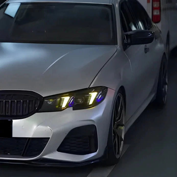 Silver BMW G20 in a garage, front three-quarter view, headlights with yellow DRL and blue insert (Snake Eyes Style)