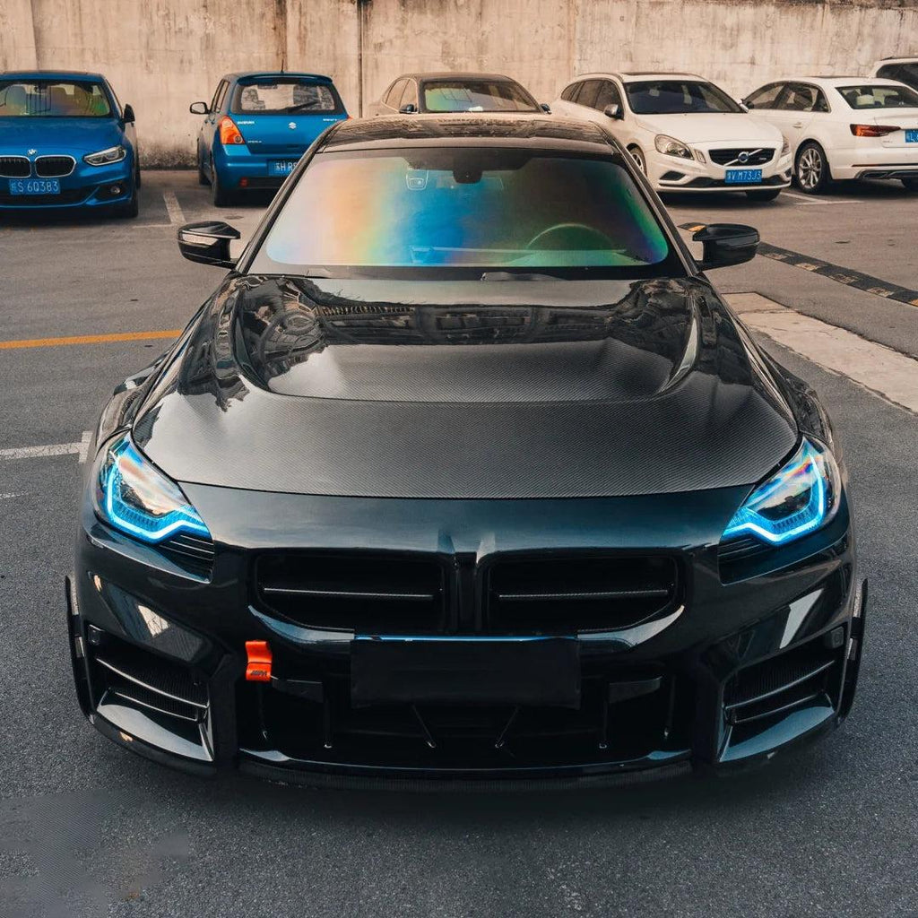 Fekete BMW G87 M2 elölről egy parkolóban, felszerelt OEM Style carbon motorháztetővel
