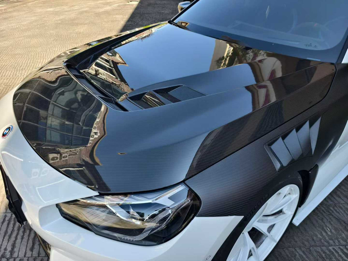 Fehér BMW G87 M2 elülső 3/4 nézetből közelről, felszerelt PM V2 Style szellőzős carbon motorháztetővel