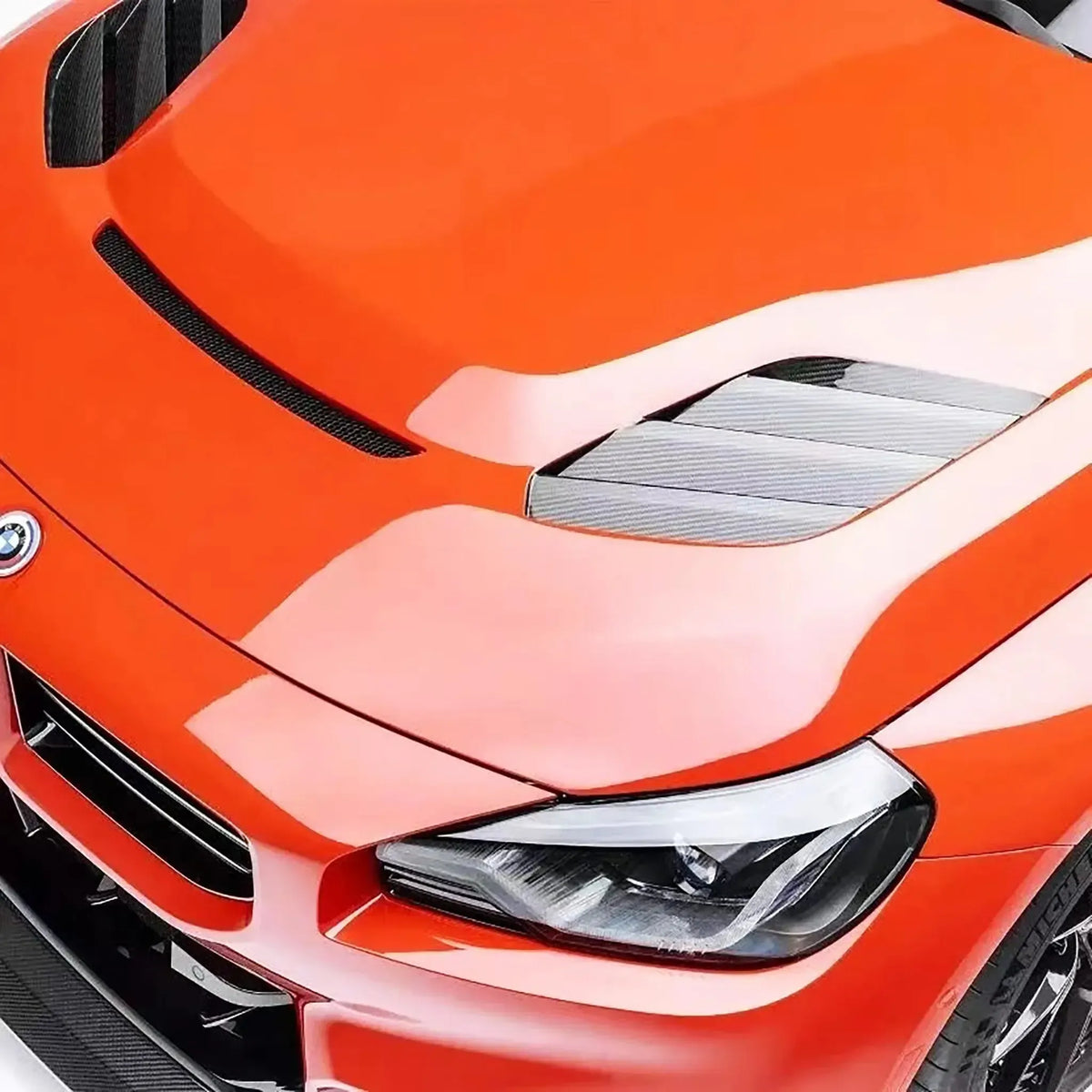 Hood of an orange BMW G87 M2, close-up, with V Style carbon side vent and front slot