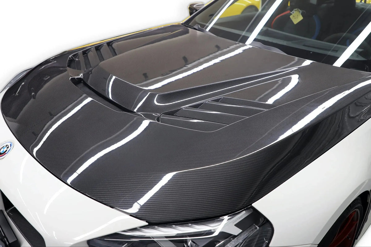 Fehér BMW G87 M2 jobb elülső 3/4 nézetből közelről, szellőzős V Style carbon motorháztetővel